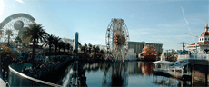 Roller coaster, ferris wheel and other amusements with a buildig in the background and water in the foreground, with a wooden walkway and metal railing in the left foreground