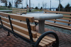 Bench with brown, 2" x 3" slats and black steel frames, with a concrete chess/checkers table between them