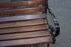 Siewalk bench with wrought iron armrest with dard wooden slats