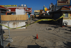 Small mostly wooden buildings surround a large whole with sand at the bottom.